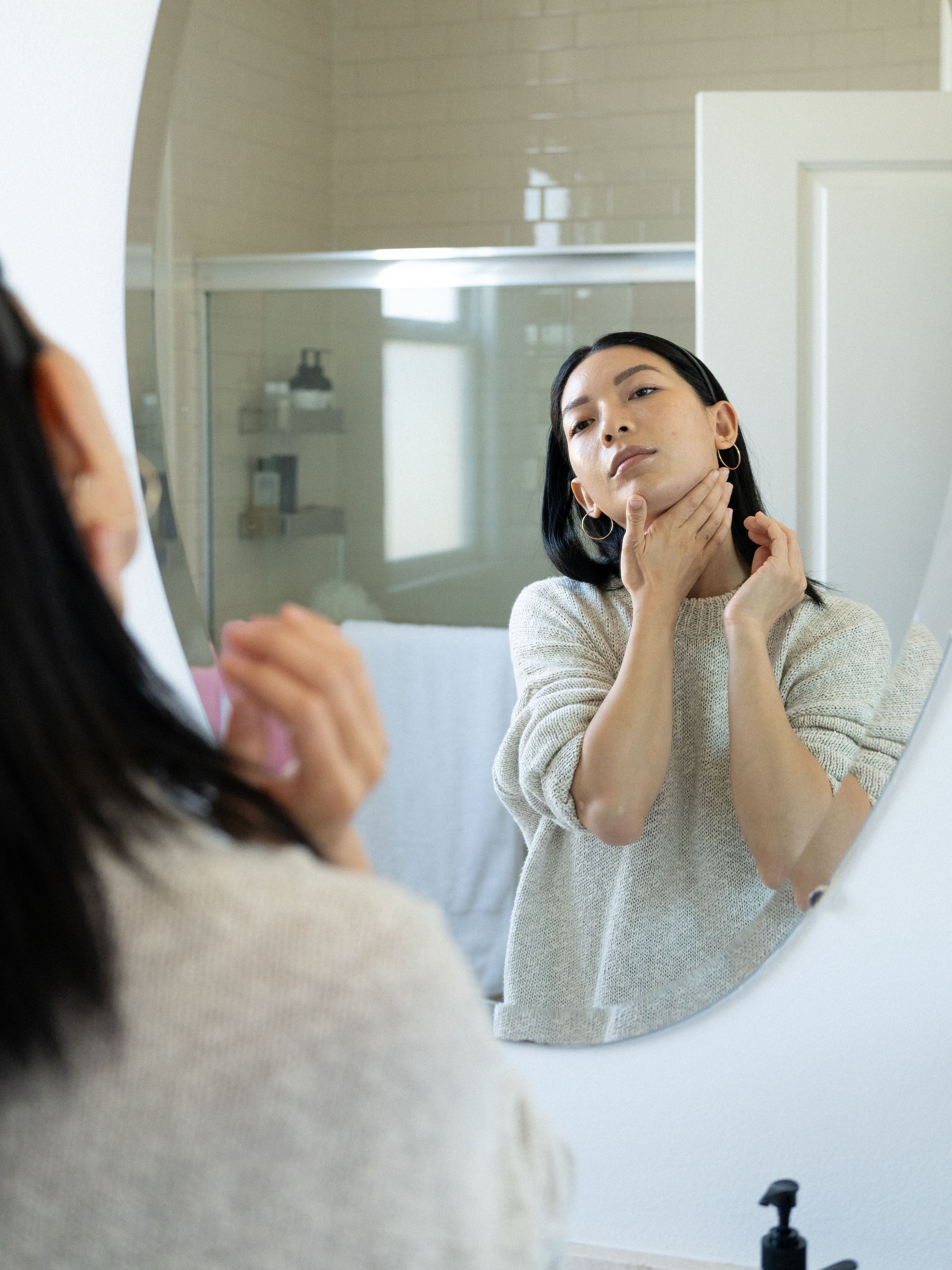 Stephanie Liu Hjelmeseth applying skincare and massaging her neck in front of a mirror.