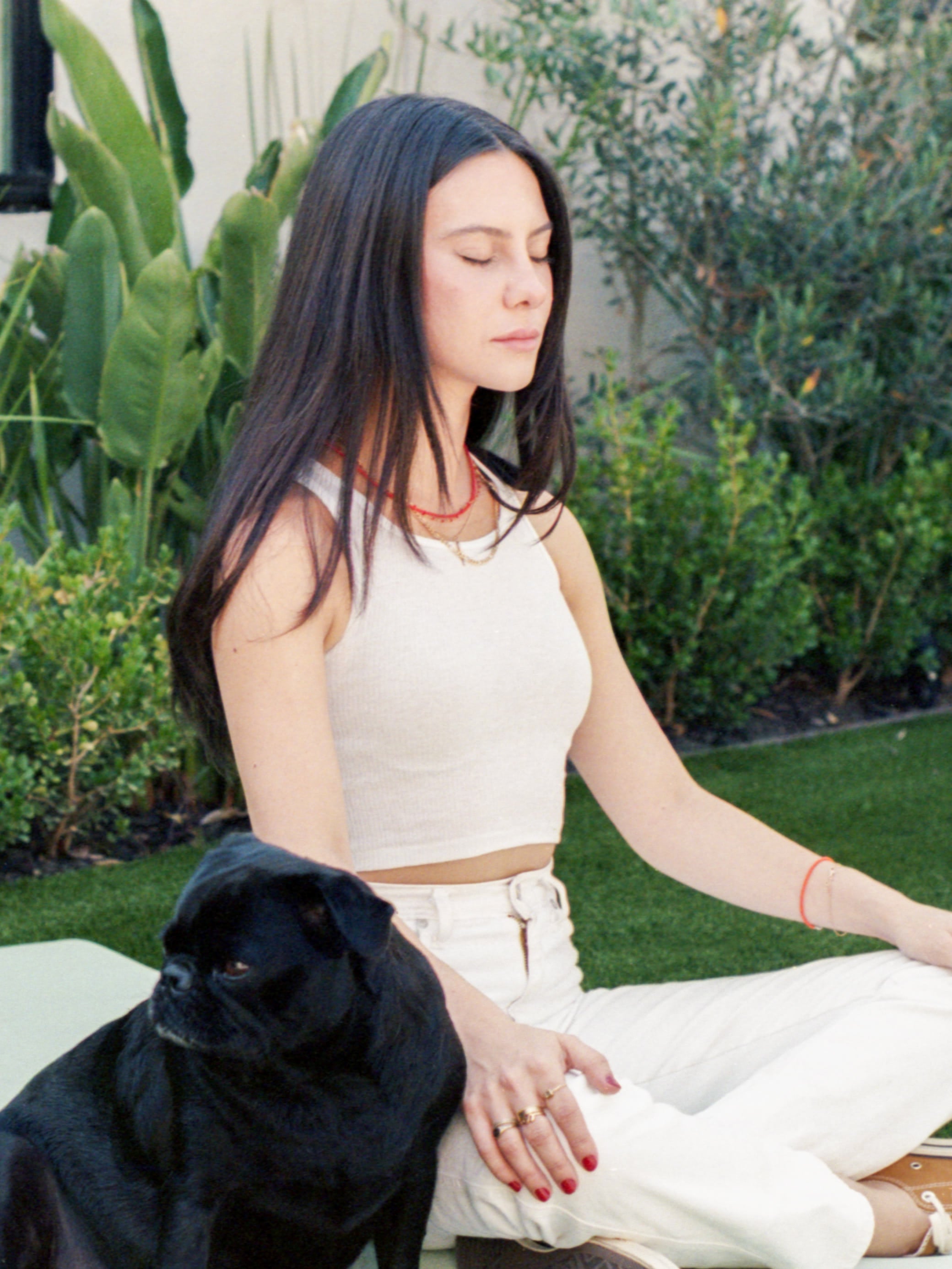 Jade Iovine meditating in the grass with her dog next to her